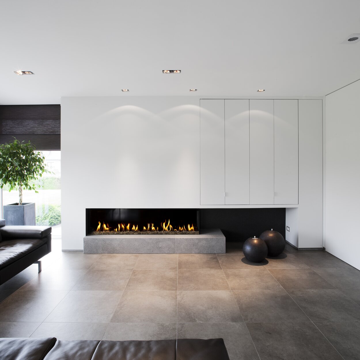 Zweiseitig verglaster Gas-Kamin G165/37C auf Betonsockel mit weisser Kaminverkleidung im modernen Wohnzimmer mit Steinboden